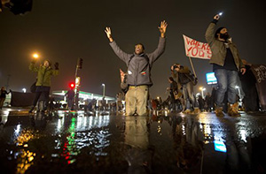 Anthony Grimes kneels on a rain-soaked street as he blocks traffic with other protesters Sunday, Nov. 23, 2014, in St. Louis. Ferguson and the St. Louis region are on edge in anticipation of the announcement by a grand jury whether to criminally charge officer, Darren Wilson in the killing of 18-year-old Michael Brown.