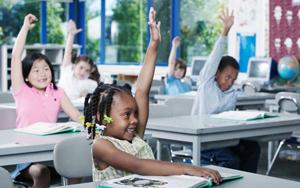 Children in a classroom raising hands to answer the teacher